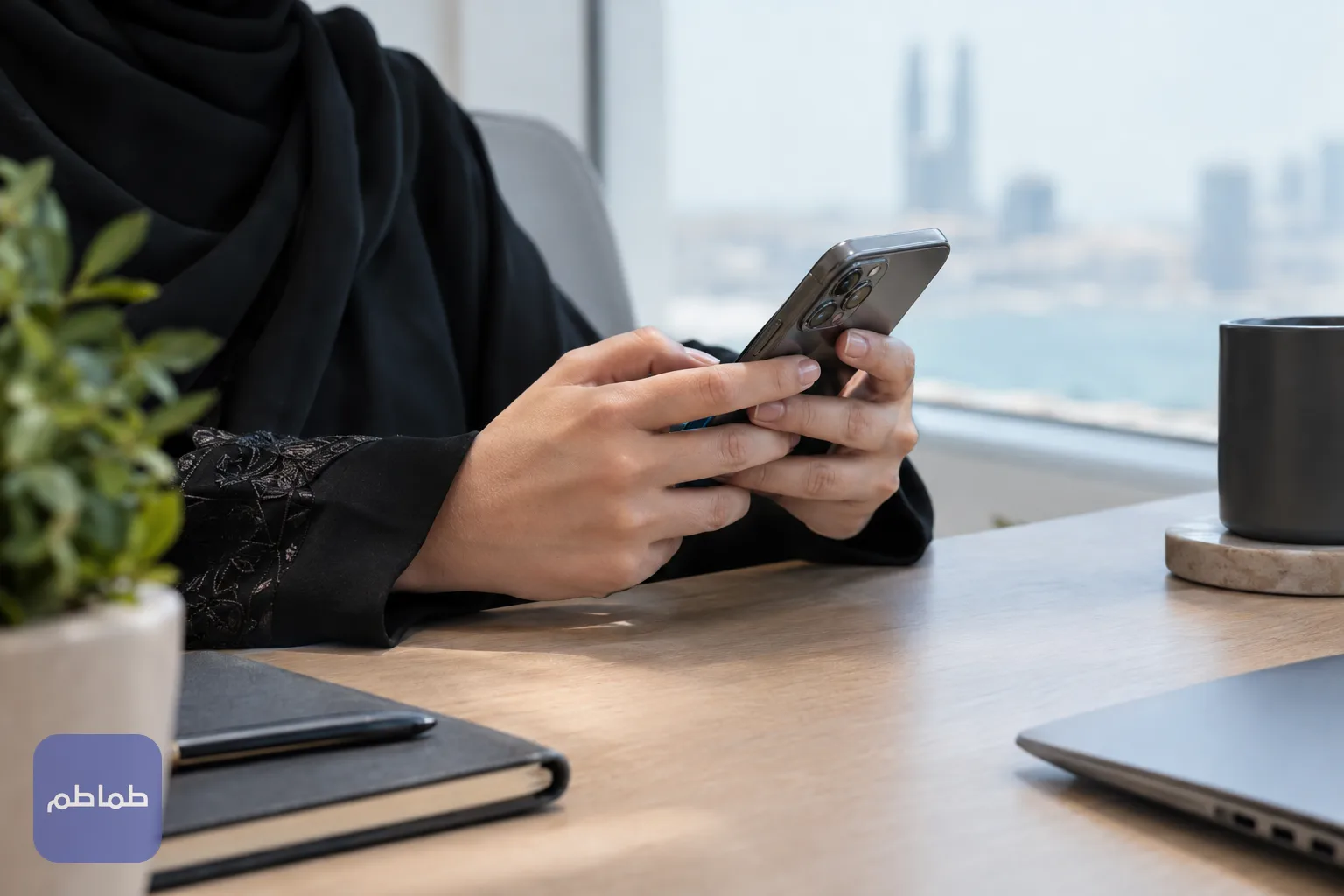 شخص يستخدم هاتفه لمراجعة خدمة إلكترونية على مكتب قرب نافذة