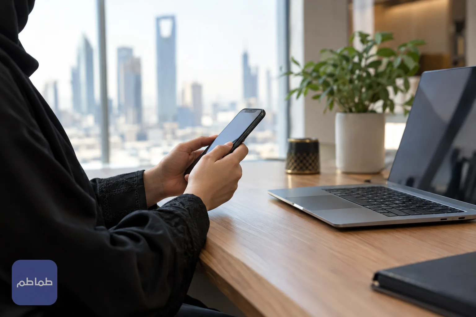 شخص يتابع إجراءً إلكترونياً عبر الهاتف والحاسوب على مكتب في مكان عمل حديث