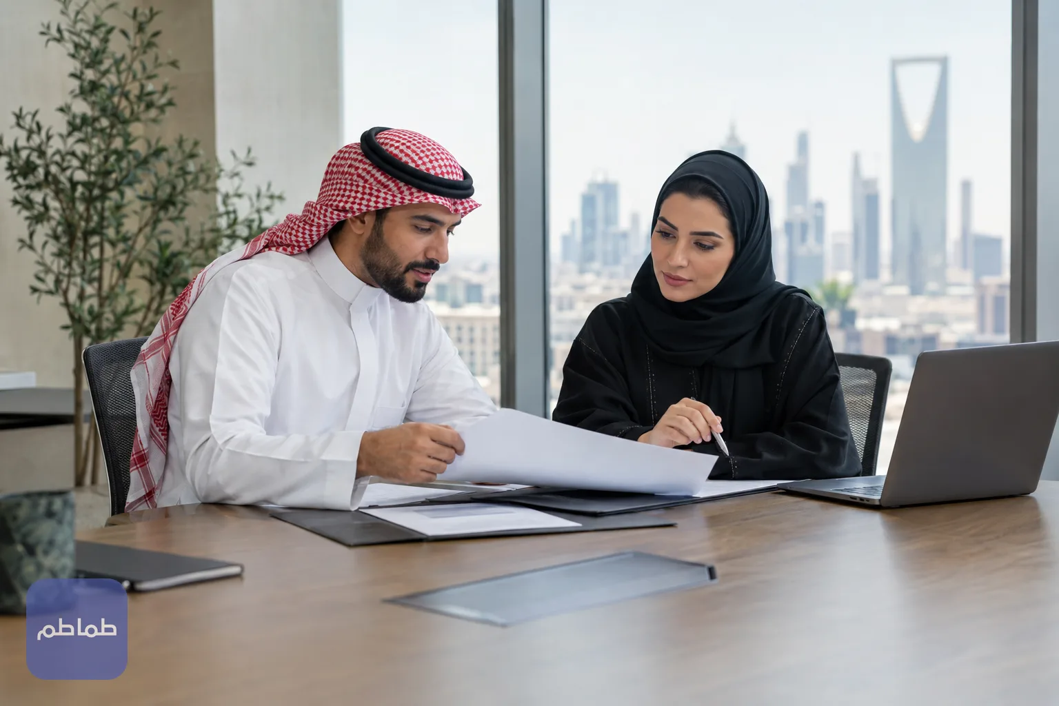 موظفان سعوديان يراجعان مستندات الرواتب والتوطين على طاولة اجتماعات في مكتب بالرياض