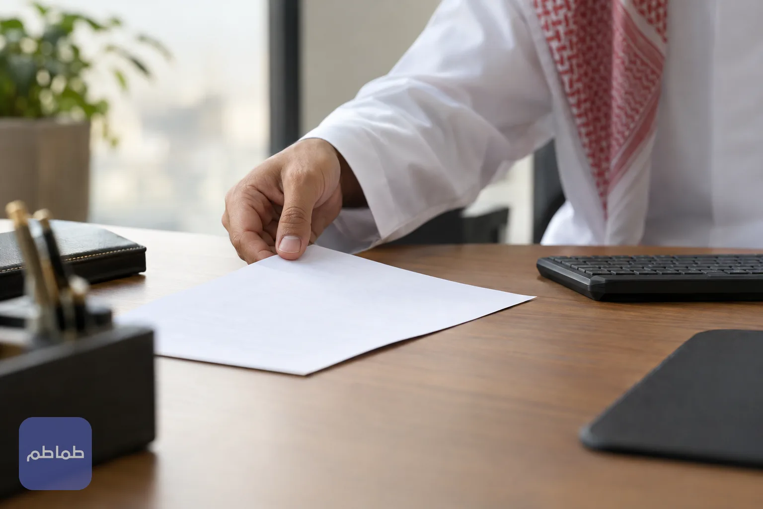 يد تضع وثيقة مطبوعة على مكتب بجانب لوحة مفاتيح
