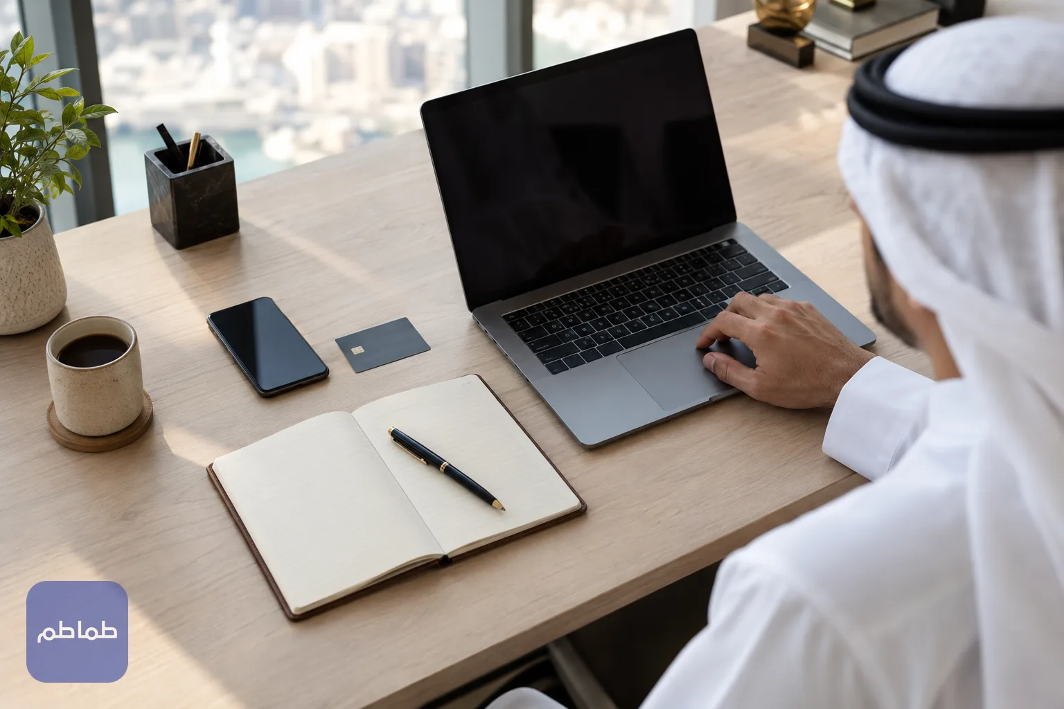 مكتب بسيط عليه حاسوب محمول وهاتف ودفتر وبطاقة دفع، يوضح تجهيز طلب إلكتروني