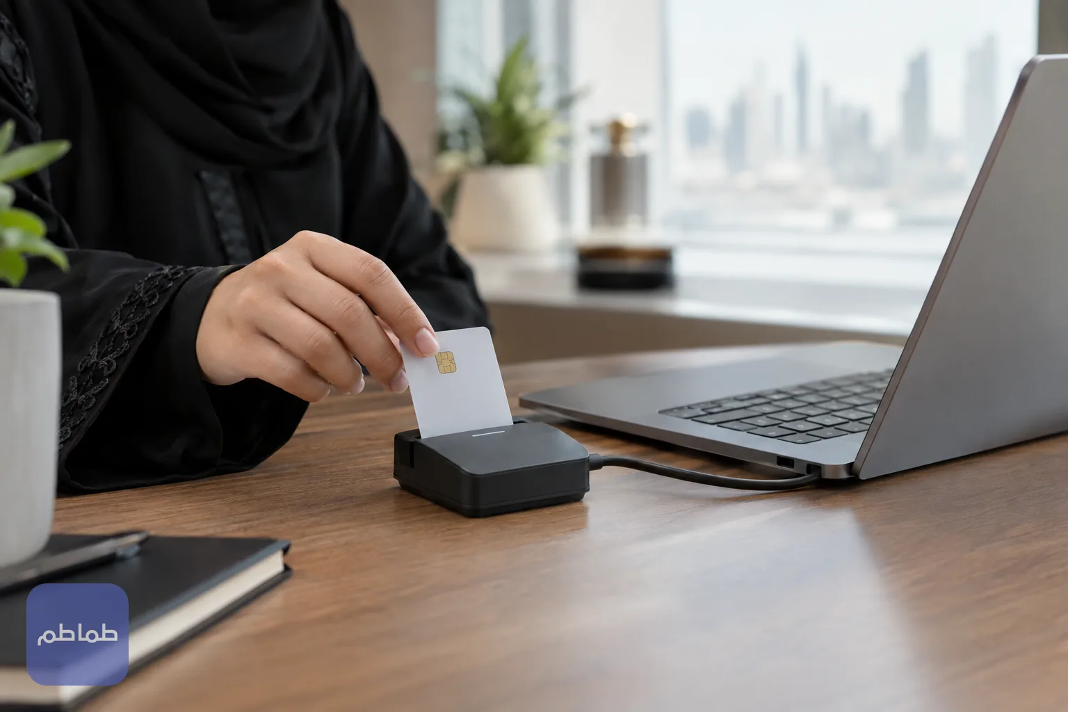 يد تُدخل بطاقة ذكية في قارئ البطاقات أمام حاسوب محمول على مكتب خشبي